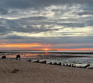 A beach with a sunset, pebbles, and a wooden structure in the foreground. - Beachfront Retreat With Panoramic Views Of The Bay (Whitstable)