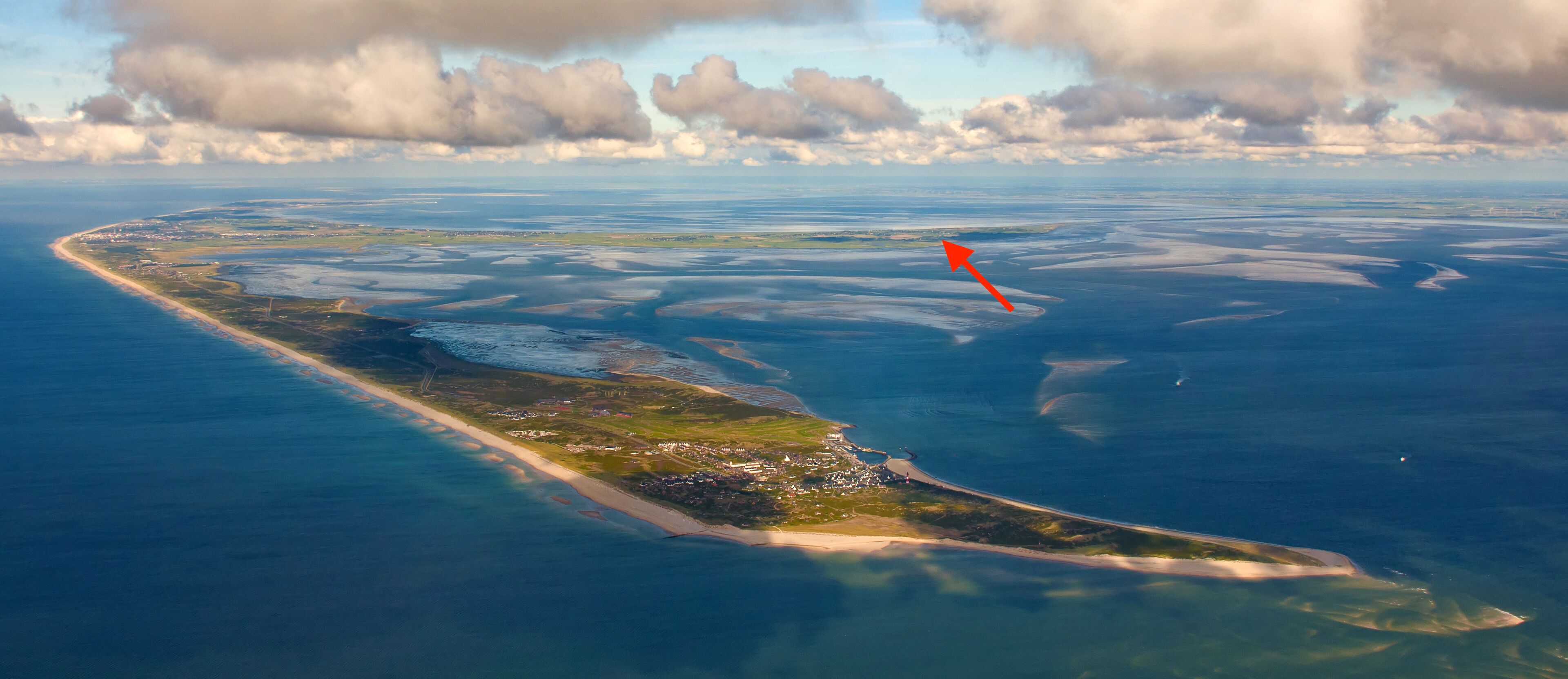 An aerial view of a coastal area with a long, narrow island featuring a mix of natural and developed areas, including a beach and scattered buildings.