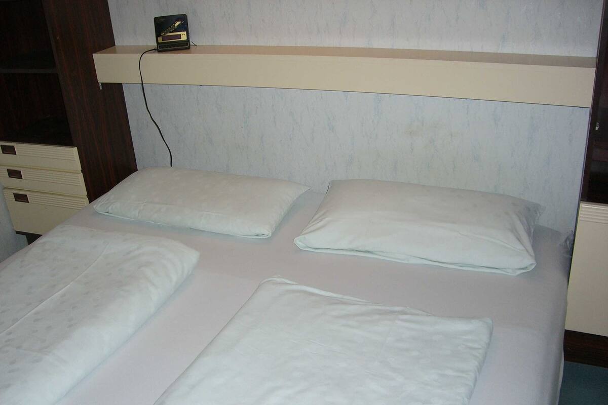 Una cama de matrimonio con ropa de cama blanca y una mesita de noche con radio.