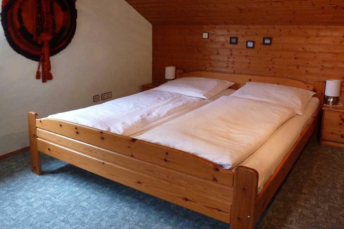 Una cama de madera en una habitación con techo inclinado y alfombra azul.