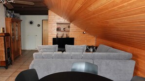 A cozy living room with a grey sofa, a wooden ceiling, a TV, and a wooden cabinet.