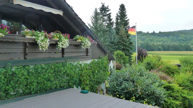 A wooden building with flower boxes on the balcony, surrounded by greenery and a flag.