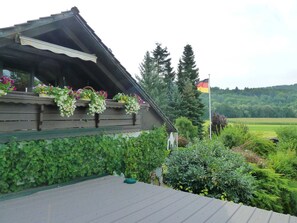 A wooden building with flower boxes on the balcony, surrounded by greenery and a flag. - Ferienwohnungen Vesteblick (Dörfles-Esbach)