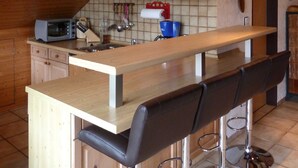 A kitchen with wooden cabinets, a microwave, a sink, and a bar area with stools.