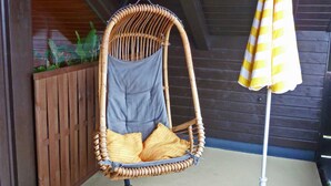A wicker chair with cushions and a white umbrella on a concrete floor.