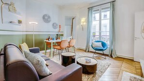 Un salon comprenant un canapé, des fauteuils, une table à manger et une fenêtre avec des rideaux.