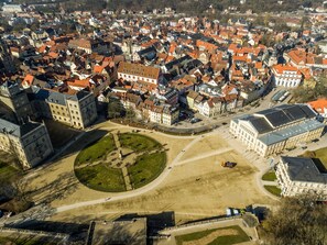 Vista aérea de uma cidade histórica com uma praça central, edifícios ao redor e uma estrutura imponente que lembra um castelo.