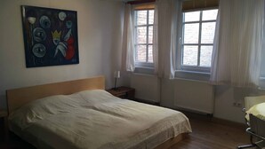 A bedroom with a bed, a painting, a window with curtains, and a radiator. - Historisches Bürgerhaus Coburg (Coburg)