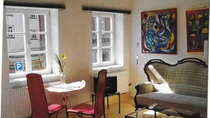 A room with a sofa, two chairs, a small table, and a radiator. There are two windows with a view of the street, and a painting on the wall. - Historisches Bürgerhaus Coburg (Coburg)