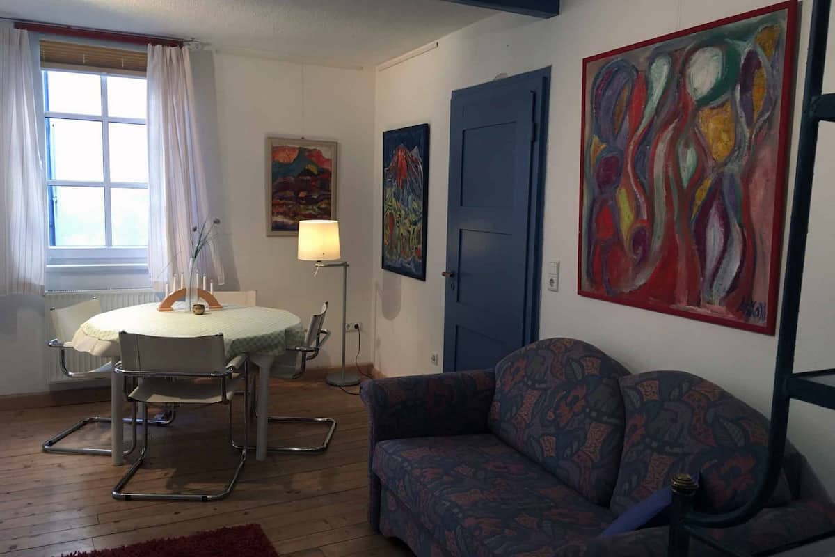 Une pièce avec une table ronde, une porte bleue, un canapé à motifs et des tableaux abstraits accrochés aux murs.