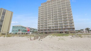 Un hotel frente a la playa con varios pisos, balcones y una zona de arena.