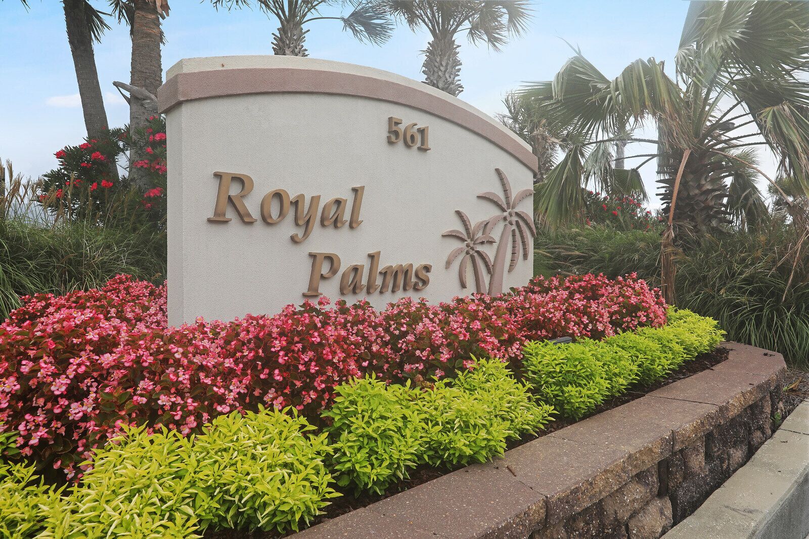 A sign for Royal Palms with the number 561, surrounded by lush greenery and palm trees.
