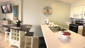 Una sala de estar con sofá, mesa de centro, televisor y una zona de cocina con microondas y estufa.
