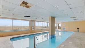 Piscina interior con vistas despejadas a la playa, un puesto de socorrista y un cartel con las normas de la piscina.
