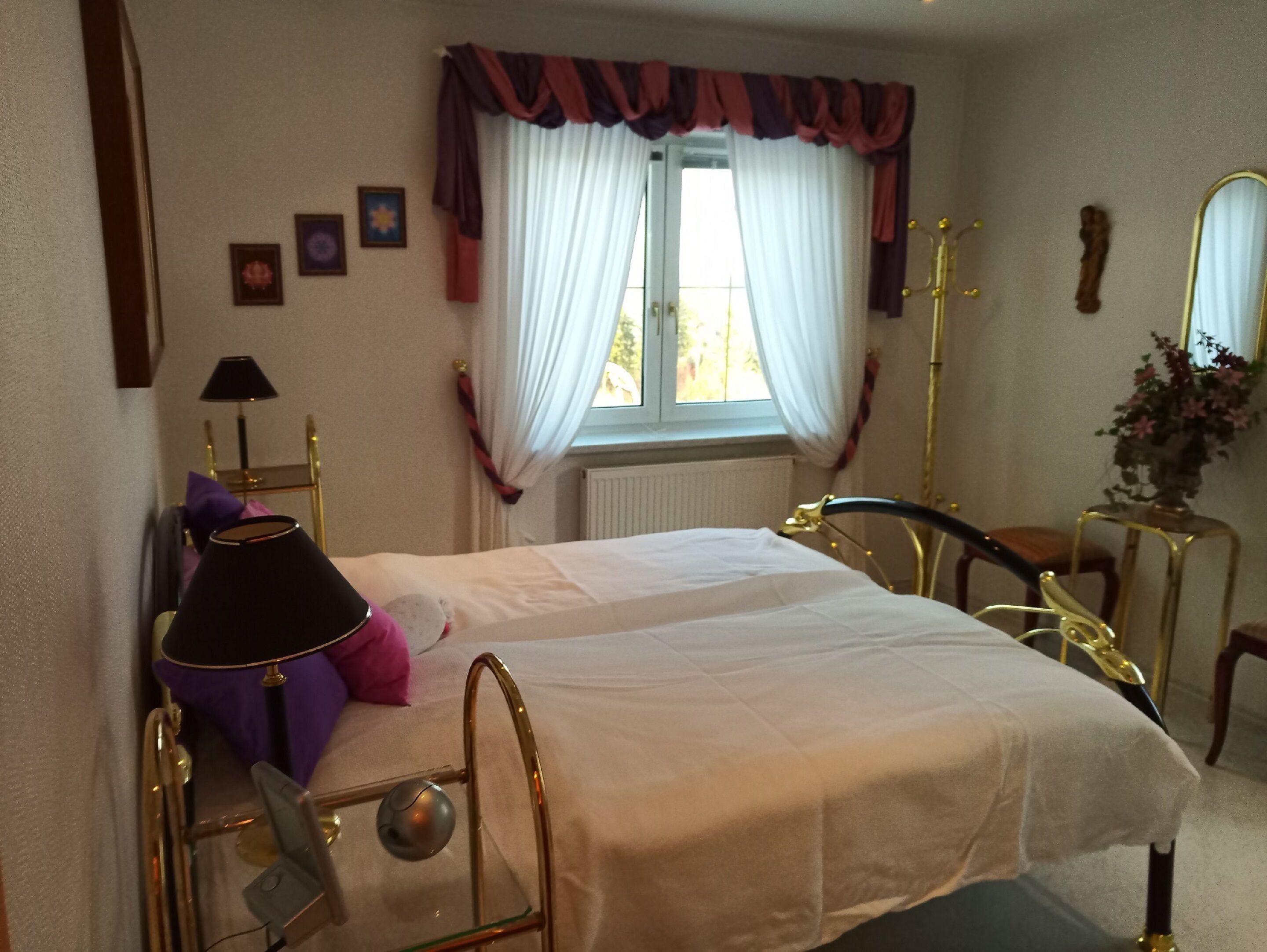A bedroom with a bed, a chair, a lamp, a radiator, and a window with curtains.