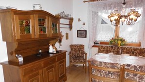 A wooden cabinet with glass doors, a patterned armchair, a dining table with a floral tablecloth, and a decorative lamp.