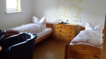 A small, well-lit room with two single beds, a wooden dresser, and a chair.