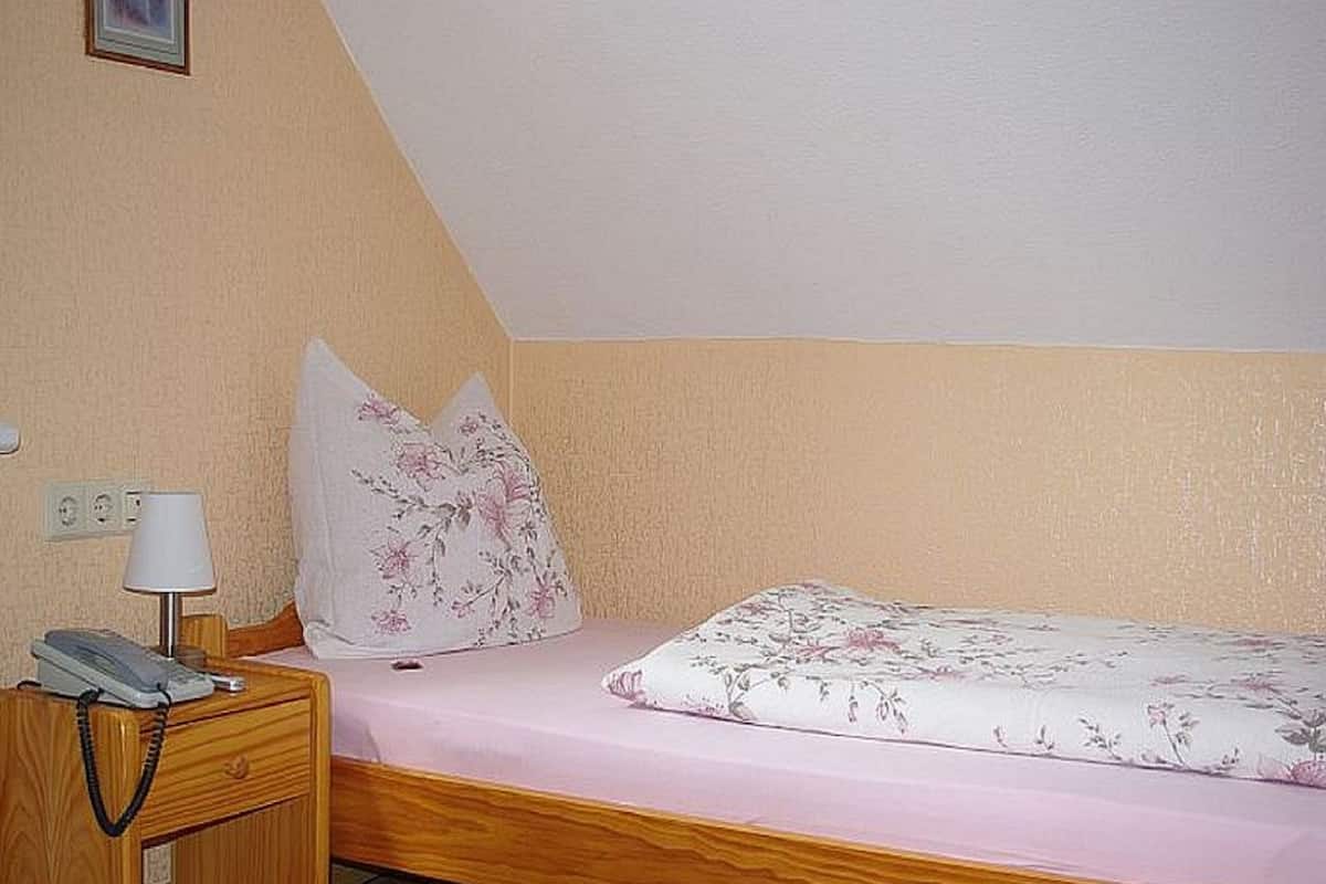 Un lit simple avec une couvre-lit à motifs floraux, dans une pièce dotée d’un plafond en pente et de meubles en bois.