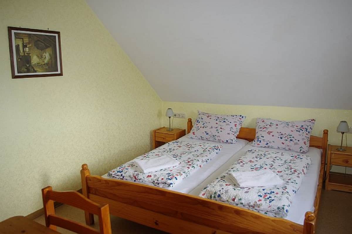 Un lit simple avec une literie à motifs floraux, une tête de lit en bois, deux tables de chevet avec des lampes et un tableau encadré au mur.