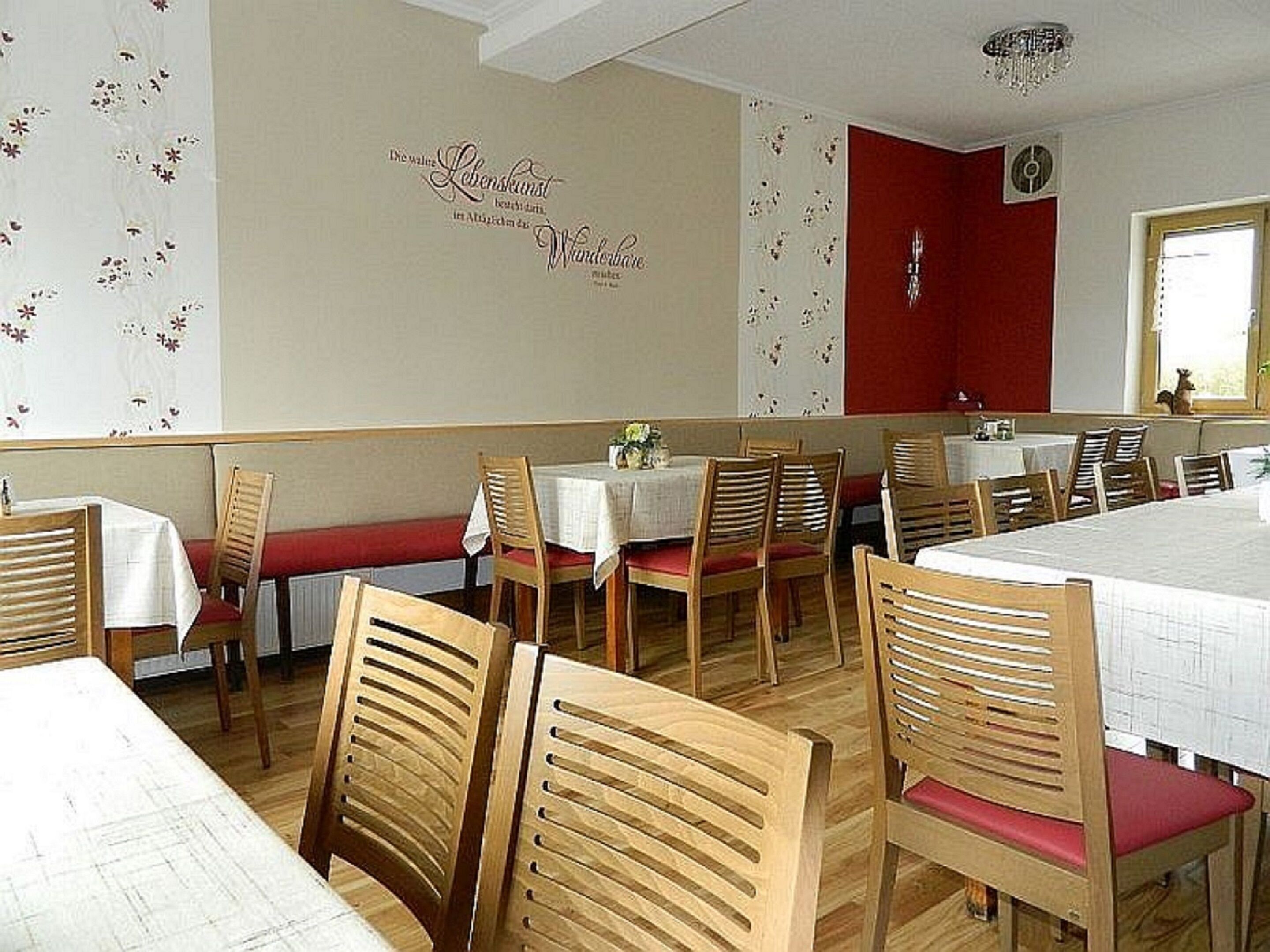 A restaurant interior with wooden chairs, white tablecloths, and floral wall decorations.