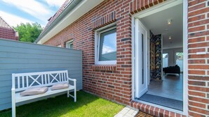 Een huis met een bakstenen gevel, een witte bank en een deur die leidt naar een interieur met een bank en een bloemenwand.