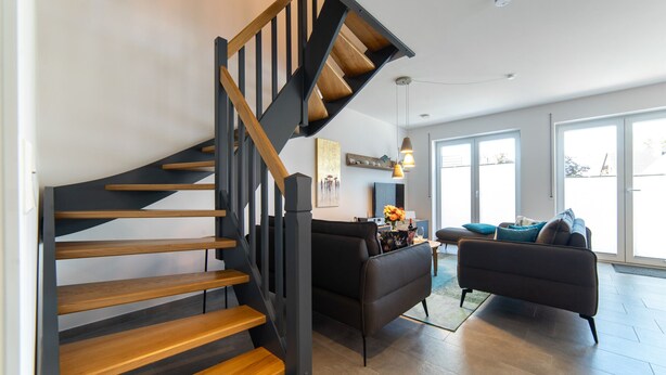 Een modern interieur met een houten trap, zwarte banken en een eethoek met een tafel en stoelen.