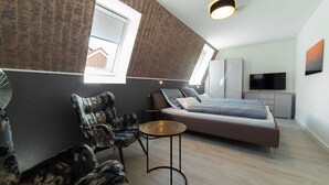 Een moderne slaapkamer met een bed, twee stoelen, een televisie en een klein tafeltje.