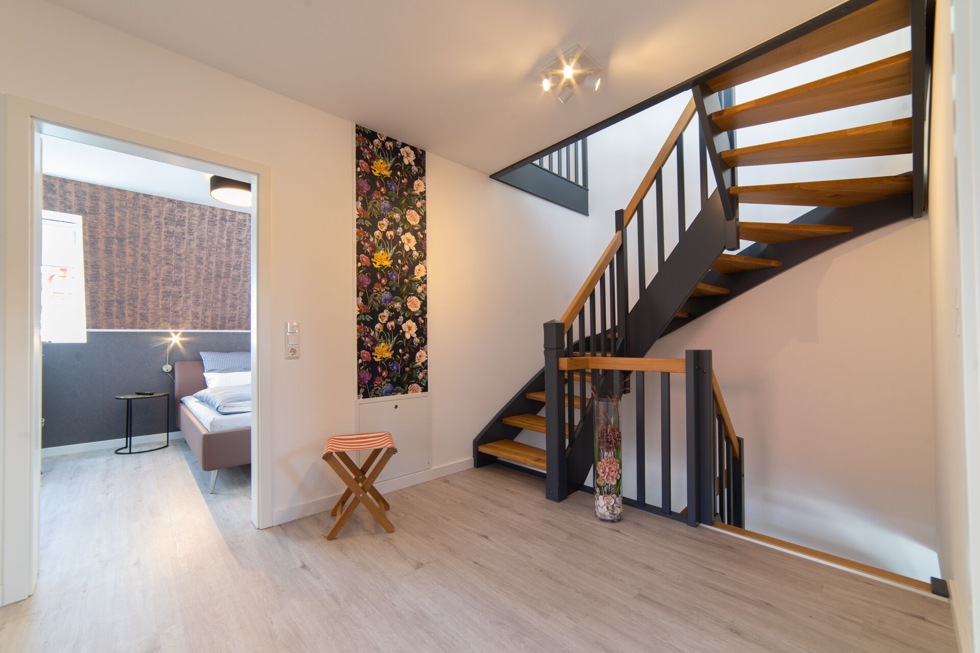 A modern interior with a wooden staircase, a small seating area with a bench, and a decorative floral wall panel.