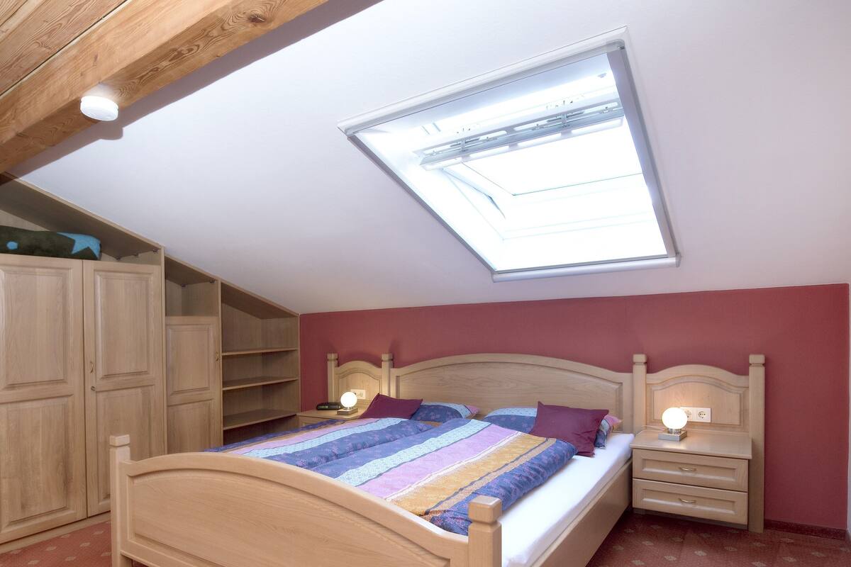 Une chambre avec un puits de lumière, un cadre de lit en bois et une table de chevet avec une lampe.