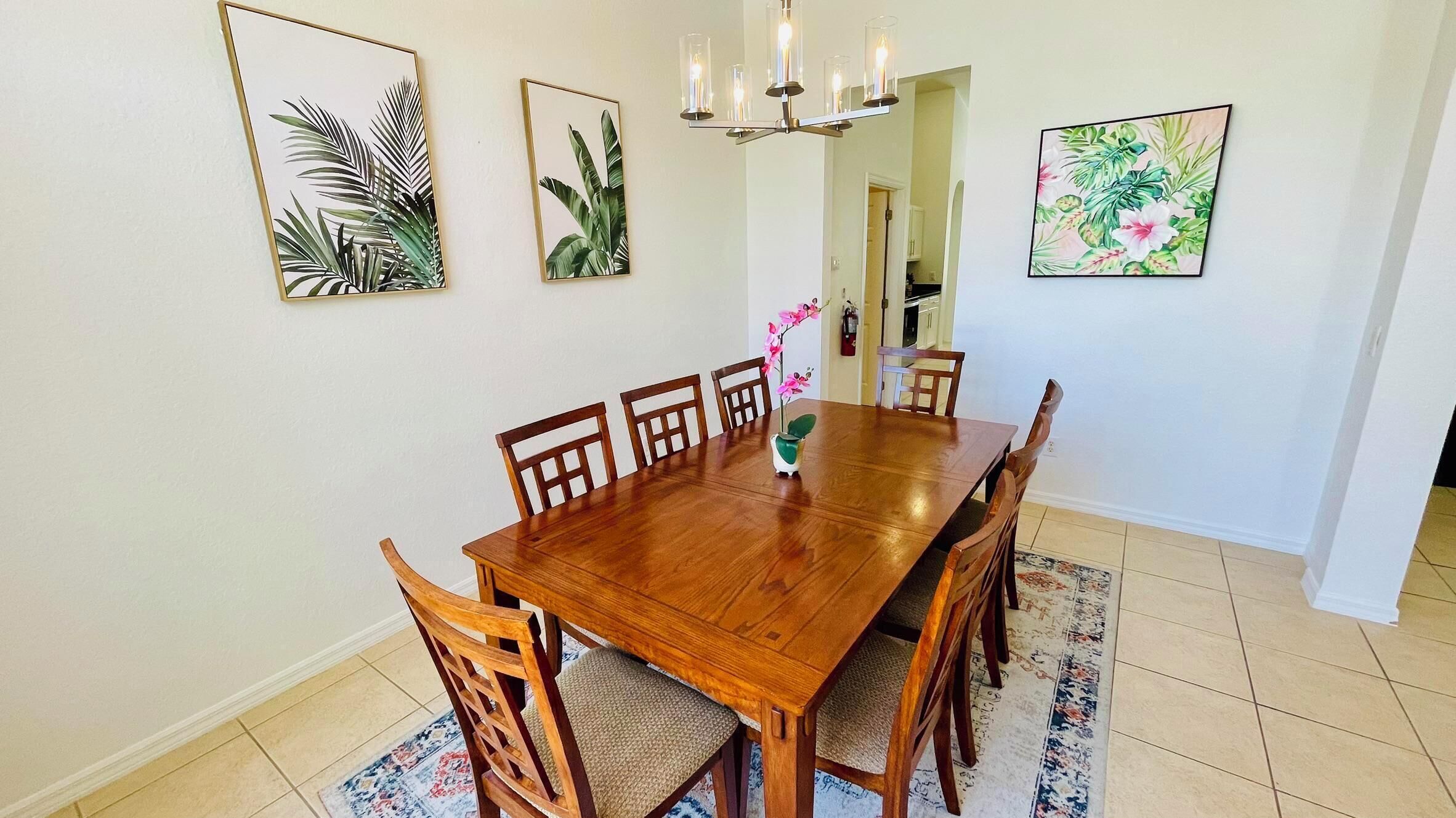 Un coin repas avec une table et des chaises en bois, agrémenté d’œuvres d’art représentant des feuilles tropicales, encadrées.