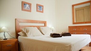 A neatly made bed with white linens, two pillows, and a blanket. There are two bedside tables with lamps, a wooden dresser with drawers, and two framed pictures on the wall. - Casa Rafa El Cotillo (El Cotillo)