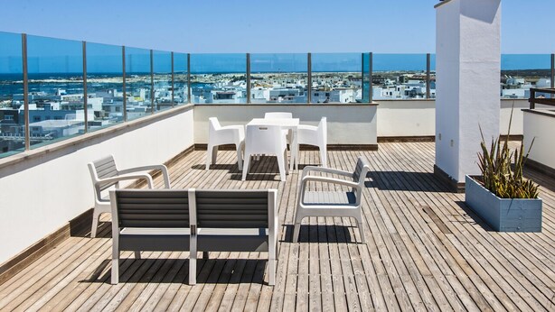 A rooftop terrace with a wooden deck, white furniture, and a view of the city and sea. - Casa Rafa El Cotillo (El Cotillo)