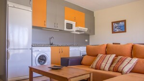 A compact living space with a kitchenette, a washing machine, a microwave, and a sofa with striped cushions. - Casa Rafa El Cotillo (El Cotillo)