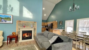 Una sala de estar moderna con chimenea, un sofá gris y una zona de comedor con sillas de madera.