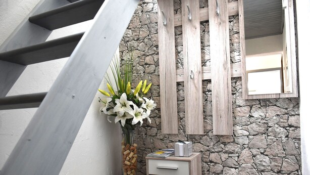 A modern interior with a stone wall, wooden cabinets, and a small wooden nightstand with a vase of flowers.