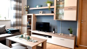 A modern living room with a flat-screen TV, wooden cabinets, a dining table, and a sofa.