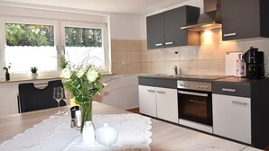 A modern kitchen with a dining table set for two, a coffee machine, and a window with a view of trees.