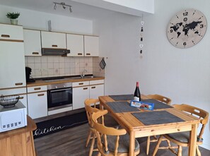 Uma cozinha moderna com armários brancos, uma mesa de jantar de madeira e um relógio com mapa mundi.
