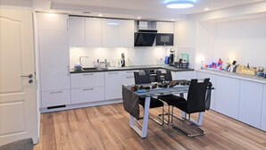 Een moderne keuken met witte kasten, een zwart aanrecht en een eethoek met een tafel en stoelen.