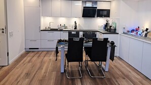 Een moderne keuken met witte kasten, een zwart aanrechtblad en een eethoek met twee zwarte stoelen.