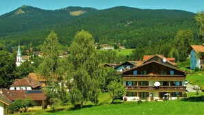 Ein traditionelles Chalet mit Balkon, umgeben von üppiger Vegetation und einer Bergkulisse.