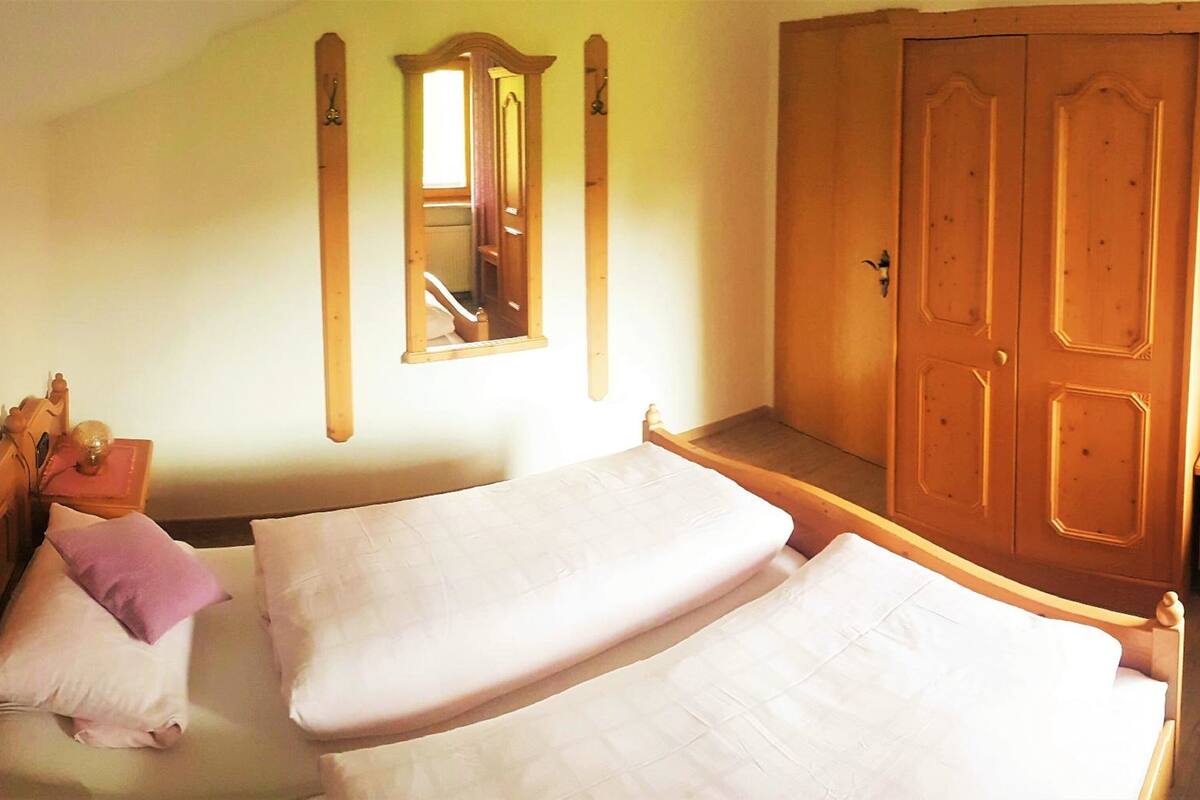 Un dormitorio con dos camas, un armario de madera, un espejo y una mesita de noche con lámpara.