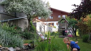 Ein Garten mit Teich, einer hölzernen Spielanlage und einer Steinmauer.