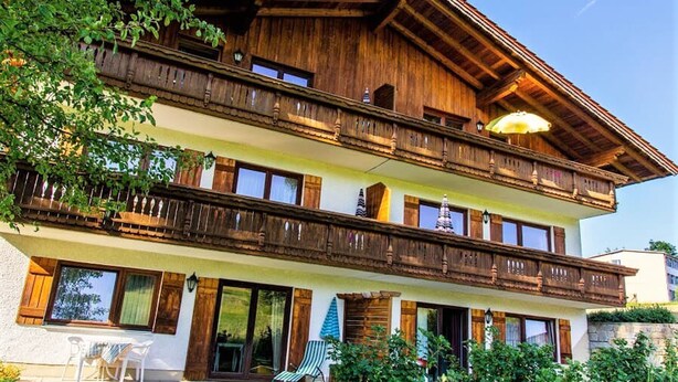 Eine zweistöckige Holzchalet mit Balkonen, großen Fenstern und Sitzgelegenheiten im Freien.
