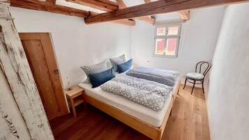 A bedroom with a wooden bed, a small bedside table, a chair, and a window with a view of the outside.