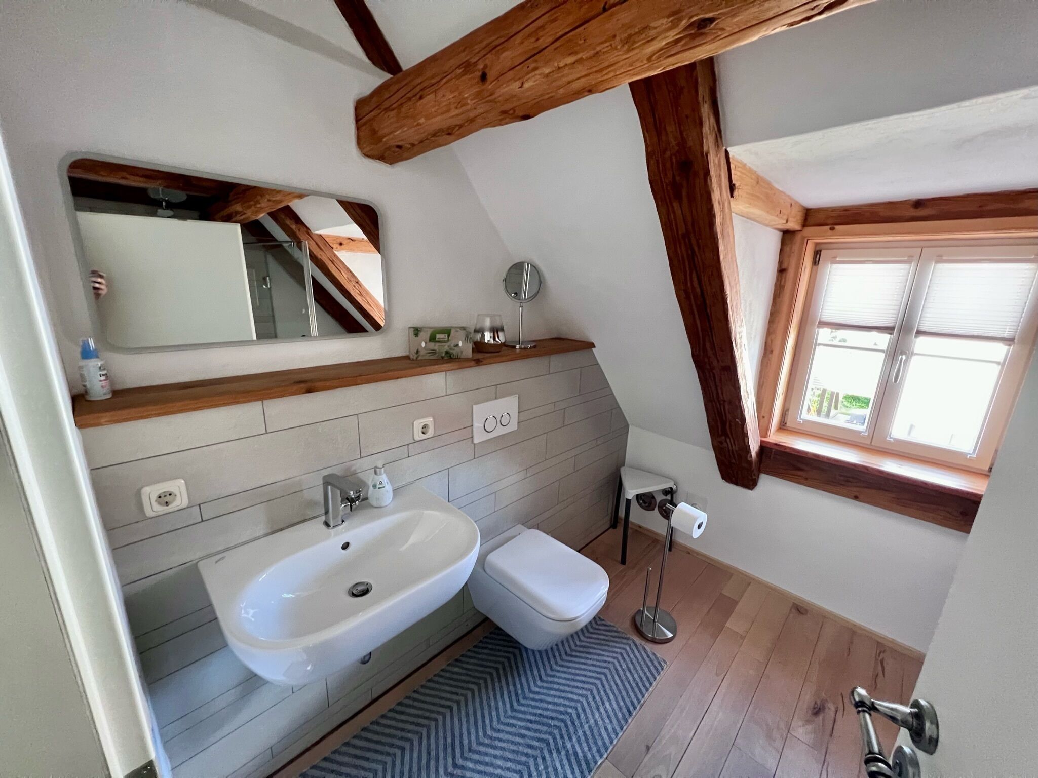 Een badkamer met een wit wastafel, toilet, spiegel en raam.