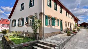 A two-story building with a red roof and green shutters, featuring a small garden with steps leading to the entrance. - Residenz Nr.6 (Zapfendorf)