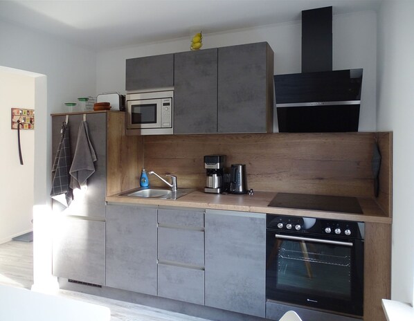 Una cocina moderna con armarios grises, microondas integrado, cafetera y horno.