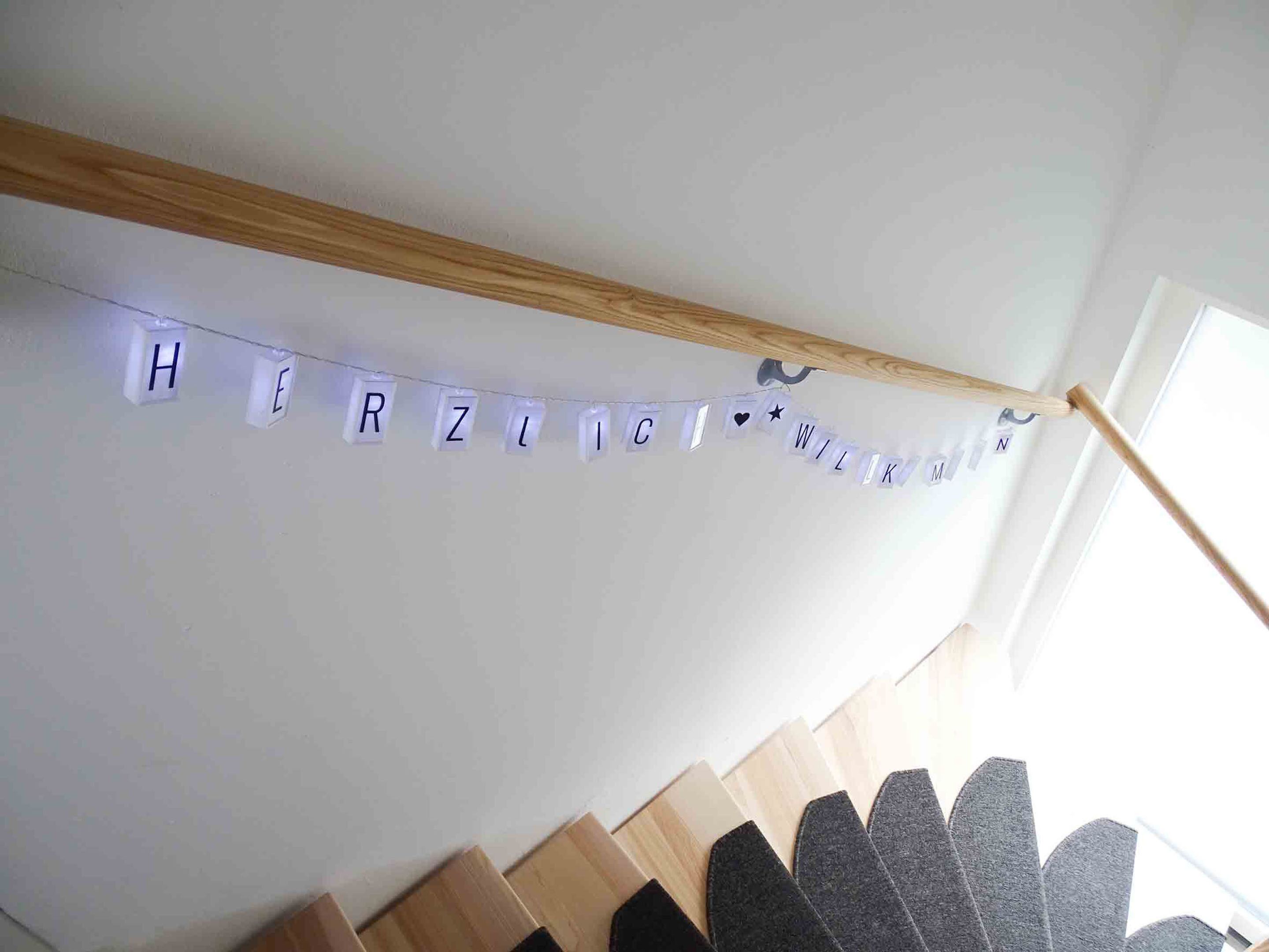 Un escalier orné d’une guirlande de lettres illuminées qui forment les mots « HERZLICH WILKOMMEN » sur un mur blanc.