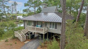 A wooden cabin with a porch and stairs, surrounded by trees and a body of water.